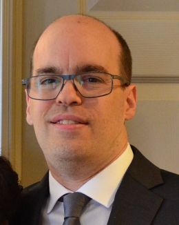 Chris Simmons wearing glasses, a dark suit and a tie